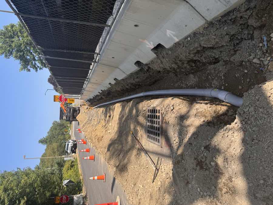 Open roadside trench with new conduit installed beside concrete barriers