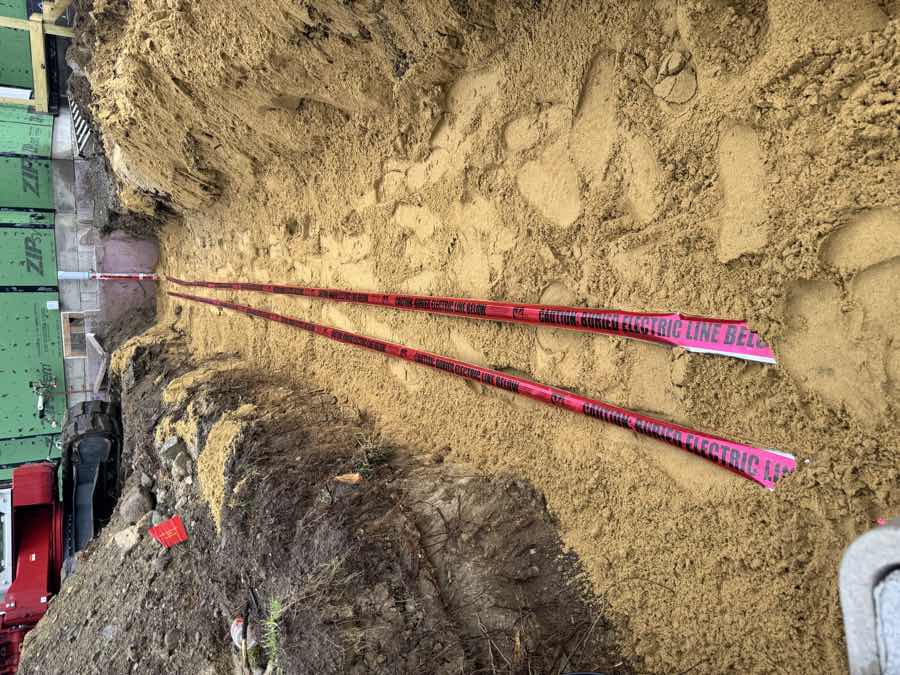 Buried electric conduit marked with red warning tape in a sand-bedded trench
